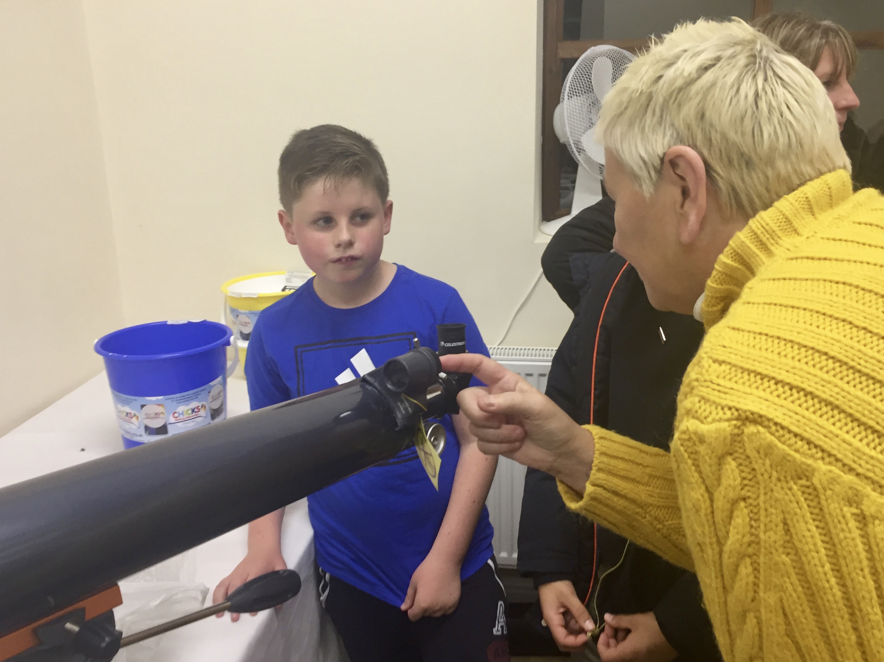 An astronomer showing a child where to look through a telescope; using the eyepiece.