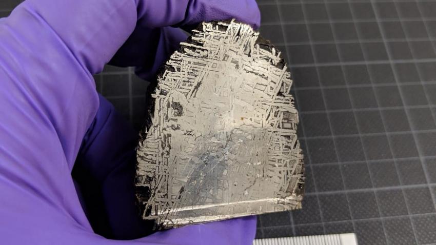 A hand holding a small meteorite showing a striated pattern on the surface