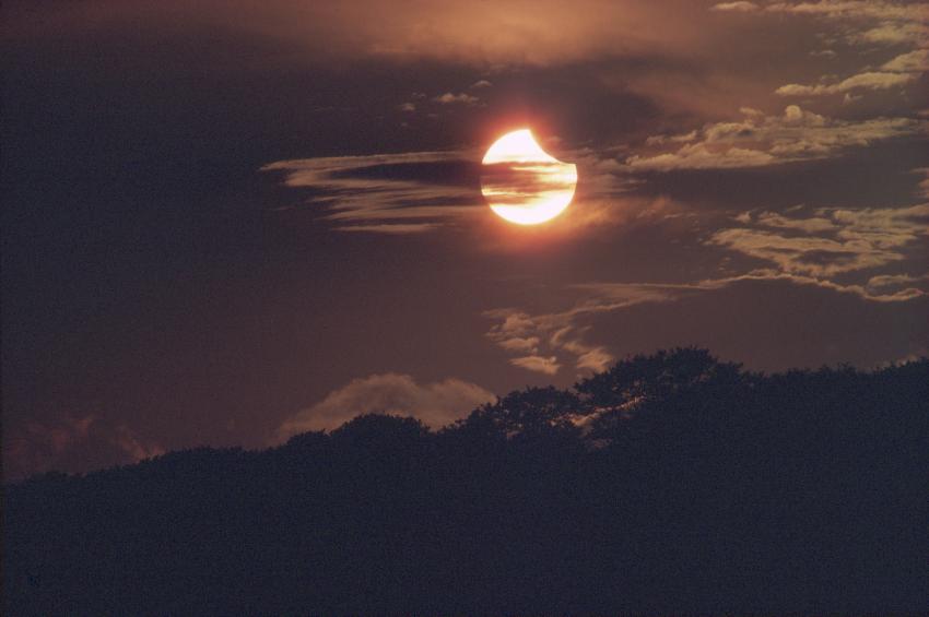 The Sun in the sky, with a 'chunk' taken out of it. This chunk is the shadow of the Moon, and it eats into the circle of the Sun, coming from the right hand side.