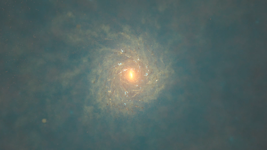 A yellow gold hued spiral galaxy against the blue-black backdrop of space.