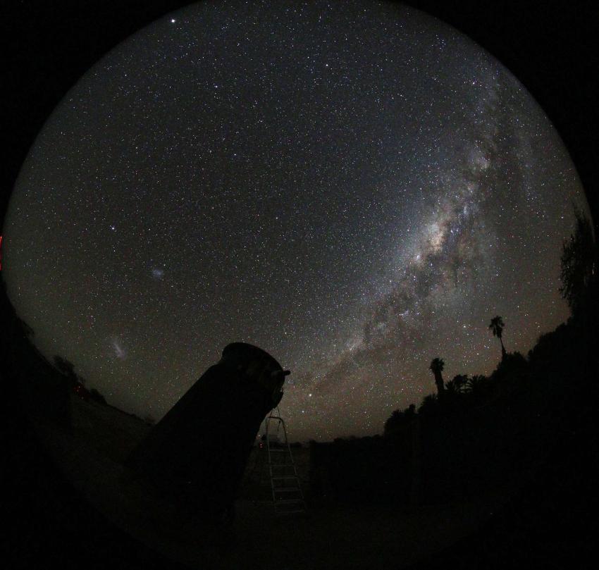 The Milky Way in the night sky. A silhouette of a telescope is visible in the foreground.