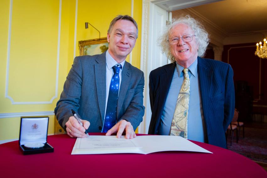 Professor Michael Kramer and Professor Mike Edmunds stand side by side behind a table covered with a red tablecloth. The Caroline Herschel Medal lies on the table to the left.