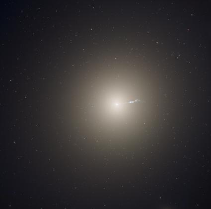 A bright white galaxy that is round in shape, glowing against the darkness of space.