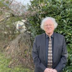 Image of Professor Mike Edmunds standing in front of trees and shrubs, smiling at the camera.