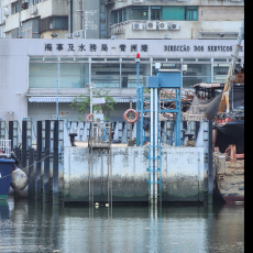 The SDV tide gauge at Macau. A wall with very obvious water markings. Behind the wall are several buildings. Water beneath the wall and markings is dark and still.