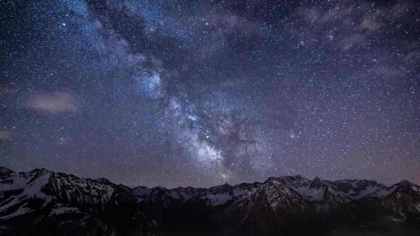 The night sky full of stars and the milky way galaxy diagonally crossing above a mountainous horizon. 