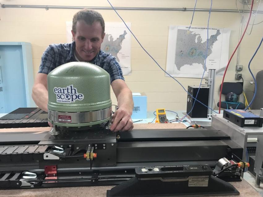 A man wearing a blue shirt working with tabletop machinery. Text on the machine reads "Earthscope".