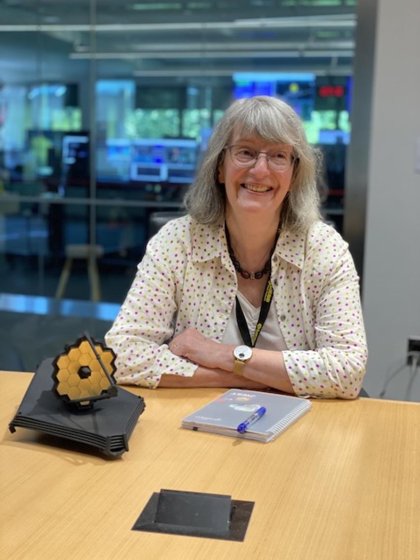 Professor Gillian Wright sitting at a table with a model of JWST
