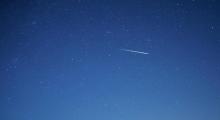 An image of a blue night sky with a single meteor visible in the centre of the frame.
