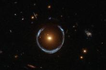 The newly discovered ultramassive blackhole lies at the centre of the orange galaxy. Far behind it is a blue galaxy that is being warped into the horseshoe shaped ring by distortions in spacetime created by the immense mass of the foreground orange galaxy.